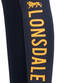 Pantaloni della tuta blu navy con il testo giallo "LONSDALE" e una grafica di leone lungo la gamba esterna, realizzati in morbido cotone.