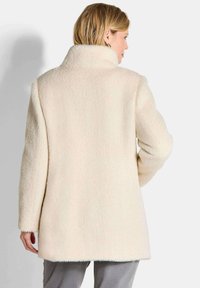 Cremefarbener, strukturierter Wollmantel mit hohem Kragen und langen Ärmeln. Verfügt über einen geraden Schnitt und dezente Nähte am Saum.