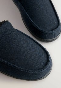 Marineblauwe wollen slippers met een visgraatpatroon, zachte textuur, ronde neus en een gestructureerde rubberen zool voor duurzaamheid.