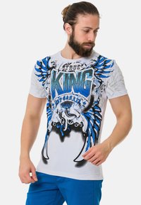 Weißes Baumwoll-T-Shirt mit blauem und schwarzem Grafikdesign, das den Text "KING" und Flügel-Motive zeigt, mit kurzen Ärmeln und Rundhalsausschnitt.