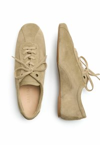 Sneakers in suede beige con punta arrotondata, chiusura con lacci, texture morbida e suola in gomma flessibile. Presentano dettagli di cucitura minimi.