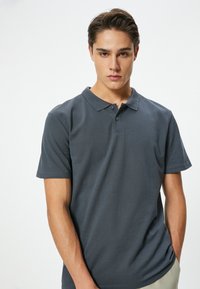 Dunkelgraues Poloshirt aus Baumwolle, mit klassischem Kragen, kurzen Ärmeln und einer Drei-Knopf-Leiste. Glatte Textur, lässige Passform.