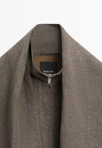 Collet de veste en tissu texturé marron avec fermeture éclair argentée et étiquette noire portant la mention "Massimo Dutti" à l'intérieur de l'encolure.