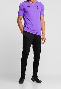 Purple Nike athletic shirt with Spurs logo, paired with black sweatpants featuring white side stripes, and black soccer cleats.