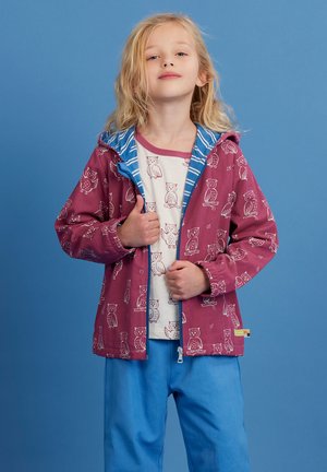 Rotete Kapuzenjacke mit weißem Eulenmuster und blauem gestreiften Futter, getragen über einem cremefarbenen Hemd. Dazu passen blaue Hosen.