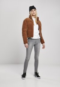 Brun kordfløyels pufferjakke med krage, hvit t-skjorte under, grå skinny jeans og svart-hvite rutete sneakers.