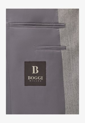 Šedá tkanina s vzorem herringbone má dvě paralelní kapsy vlevo. Na ní je vyšitá černá nálepka s nápisem "BOGGI MILANO" v bílé barvě.