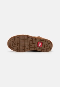 Suela de goma marrón con un patrón texturizado, que presenta un logo rojo y un detalle circular cerca del talón. Diseño robusto y plano.