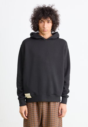 Black hoodie made of sweatshirt material, featuring a simple design, long sleeves, and a small label detail at the hem.