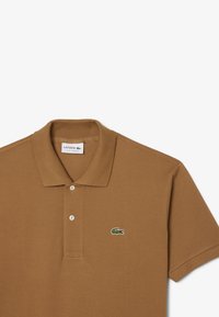 Hnědá polokošile z texturované tkaniny, s límečkem, dvěma knoflíky a zeleným vyšívaným logem krokodýla na levé straně hrudi.