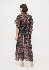 Gjennomsiktig, blomstret kimono i mørk marineblå med rosa og grønne botaniske mønstre. Løs passform, ankellengde, kortermet og lett stoff.
