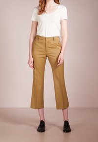 Beige högmidjade byxor med skräddarsydd passform, utsvängda från knäet, i kombination med en vit åtsittande t-shirt och svarta platta skor.