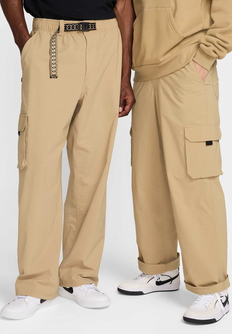Beżowe spodnie cargo z elastycznym pasem i ozdobnym paskiem. Posiadają boczne kieszenie i luźny krój. W połączeniu z bia�łymi butami.