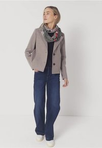Blazer gris claro con dos botones, combinado con jeans de pierna ancha en azul oscuro, zapatillas blancas y una bufanda de varios patrones en colores variados.