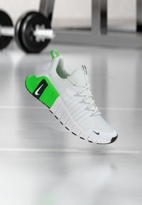 White athletic shoe with green accents, textured upper, black outsole, and signature swoosh logo. Laces and padded collar visible.
