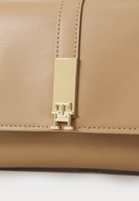Beżowa skórzana torba o gładkiej fakturze, z zapięciem w kolorze złota oraz subtelnymi przeszyciami wzdłuż krawędzi.