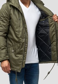 Zielona oliwkowa kurtka ocieplana z kapturem, z zamkiem błyskawicznym i zapięciem na zatrzaski, oraz czarną pikowaną podszewką.