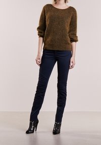 Brązowy, futrzasty sweter z trzyczwartowymi rękawami, w połączeniu z dopasowanymi granatowymi spodniami. Czarne, lakierowane, wysokie botki dopełniają całość.