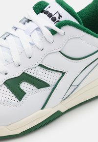 Valkoiset lenkkarit vihreillä yksityiskohdilla, valmistettu sileästä nahasta. Varustettu rei'itetyillä osilla, tasaisilla nauhoilla ja pehmustetulla nilkkapohjalla. Kumipohja.