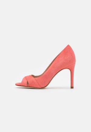 Koraalroze suède pumps met hoge hak, open teen en slanke hak, zijaanzicht op witte achtergrond.