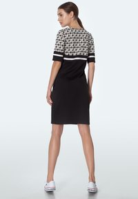 Czarna sukienka z krótkimi rękawami, ozdobiona wzorem w pieszy ząb w odcieniach szaro-białych na górze, gładka tkanina, długość do kolan, z bocznymi rozcięciami.