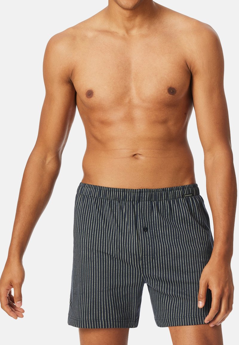 Raidallinen tummansininen miesten bokserihousu, joissa on valkoiset pystyrivit, joustava vyötärö ja etupainike. Pehmeä kangas.