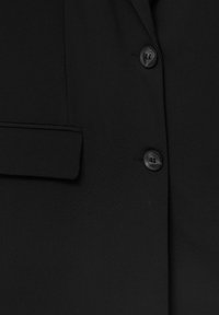 Veste noire en tissu lisse avec un col cranté, une poche poitrine unique et deux boutons noirs sur le devant.