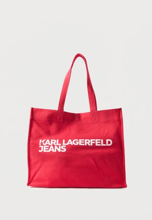 Rød stoffveske med to håndtak og fet hvit «KARL LAGERFELD JEANS»-tekst foran mot ensfarget bakgrunn.