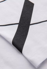Hvid t-shirt med teksturerede sorte og gyldne detaljer. Designet inkluderer fede grafiske linjer og et glat, blødt stof.