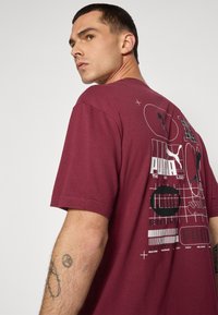Bordeaux kortærmet t-shirt lavet af bomuld, med grafisk print på ryggen med logo mønstre og gitterdesign i hvid og sort.