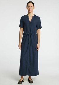 Robe maxi bleu marine à manches courtes avec un col en V, une taille à cordon et une coupe droite. Tissu texturé avec un minimum de détails.