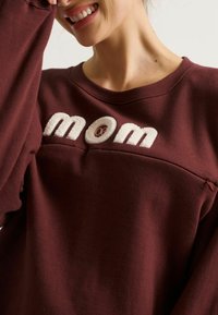 Bordeaux sweatshirt met geborduurde "mom" tekst in crème, met een zachte textuur en ronde hals. Eenvoudig ontwerp met minimale details.