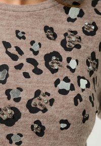 Brązowy sweter z czarnym i srebrnym nadrukiem w panterę oraz teksturowymi akcentami. Ozdobiony metalowymi ćwiekami i cekinami. Miękki materiał.