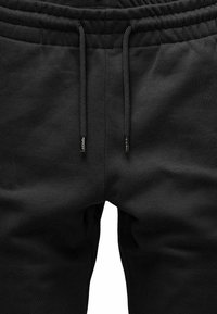 Schwarze Sweatpants aus einem weichen Stoff, mit einem elastischen Bund und Kordeln mit Metallspitzen. Schlichtes Design, keine Muster.