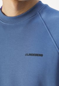 Blå sweatshirt med strukturerad yta. Har en rund halsringning och en diskret svart logga på bröstet. Utrustad med raglanärmar för extra komfort.