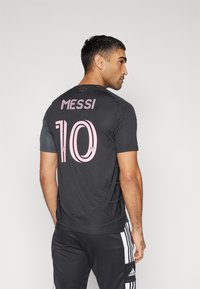 Svart sportströja med "MESSI" och nummer "10" tryckt i rosa. Korta ärmar, rund halsringning, tillverkad av lätt material.