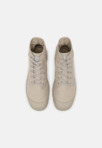 Paire de baskets montantes en toile beige avec lacets, vues de dessus sur un fond gris clair uni.