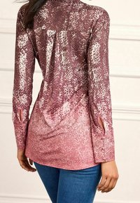Maglietta a maniche lunghe con una gradazione di bordeaux a rosa, caratterizzata da un motivo a macchie, maniche con risvolto e dettagli con bottoni. Tessuto morbido e leggero.