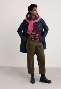 Mornarska parka s krznom, burgundska kordura košulja, prugasti ružičasti i ljubičasti top, maslinaste kordura hlače, ružičasti šal, crne čizme do gležnjeva.