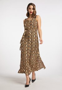 Brązowa i czarna maxi sukienka w wzór w węża z cienkimi ramiączkami, paskiem w talii i swobodnym dołem. Noszona z czarnymi szpilkami.