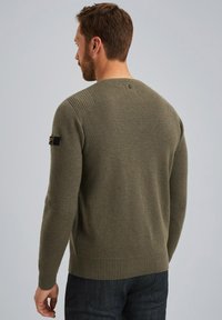 Olivgrüner Strickpullover mit geripptem Saum und Bündchen, der ein strukturiertes Muster und ein kleines schwarzes Logo-Patch auf der linken Schulter aufweist.