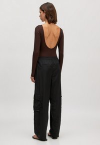 Langmouw bruin bodysuit met diepe rug, gecombineerd met zwarte satijnen cargobroek met zijzakken en een elastische tailleband.