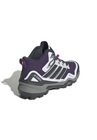 Chaussure de randonnée violet et noir avec accents blancs, en matériau synthétique texturé, semelle en caoutchouc épaisse et design à lacets. Comprend une boucle au talon.