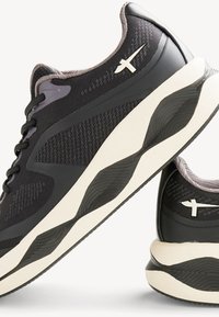 Black athletic shoes with a textured upper, contrasting light accents, and a thick white midsole featuring a wavy pattern and logo detail.