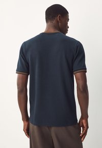 T-shirt a maniche corte blu navy con collo a coste e strisce a contrasto. Tessuto strutturato; vestibilità comoda; design minimalista.