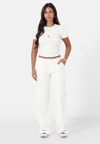 Witte cropped t-shirt met een klein rood logo, gecombineerd met witte baggy cargo pants met zijzakken en een elastische tailleband.