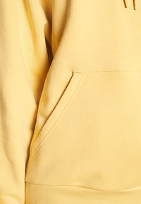 Yellow hoodie featuring a front kangaroo pocket, soft texture, ribbed cuffs, and a drawstring hood.