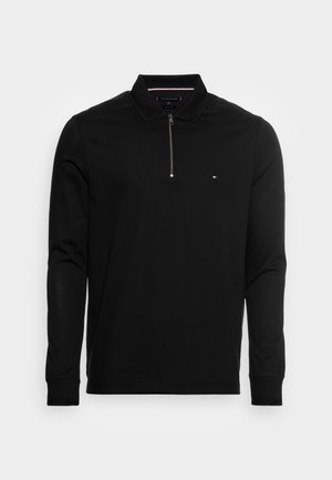 Polo nera a maniche lunghe con mezza zip frontale, piccolo logo Tommy Hilfiger sul petto sinistro e polsini a coste.
