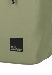 Groene stoffen tas met een zwart vierkant logo en de tekst "Jack Wolfskin" in lichtgrijs, met een gestructureerd oppervlak en een trekkoordsluiting.
