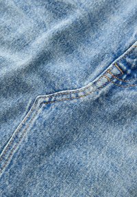 Ljust blå denimtyg med en texturerad yta, med orange sömmar och detaljsömmar, vilket visar naturliga veck och skrynklor.